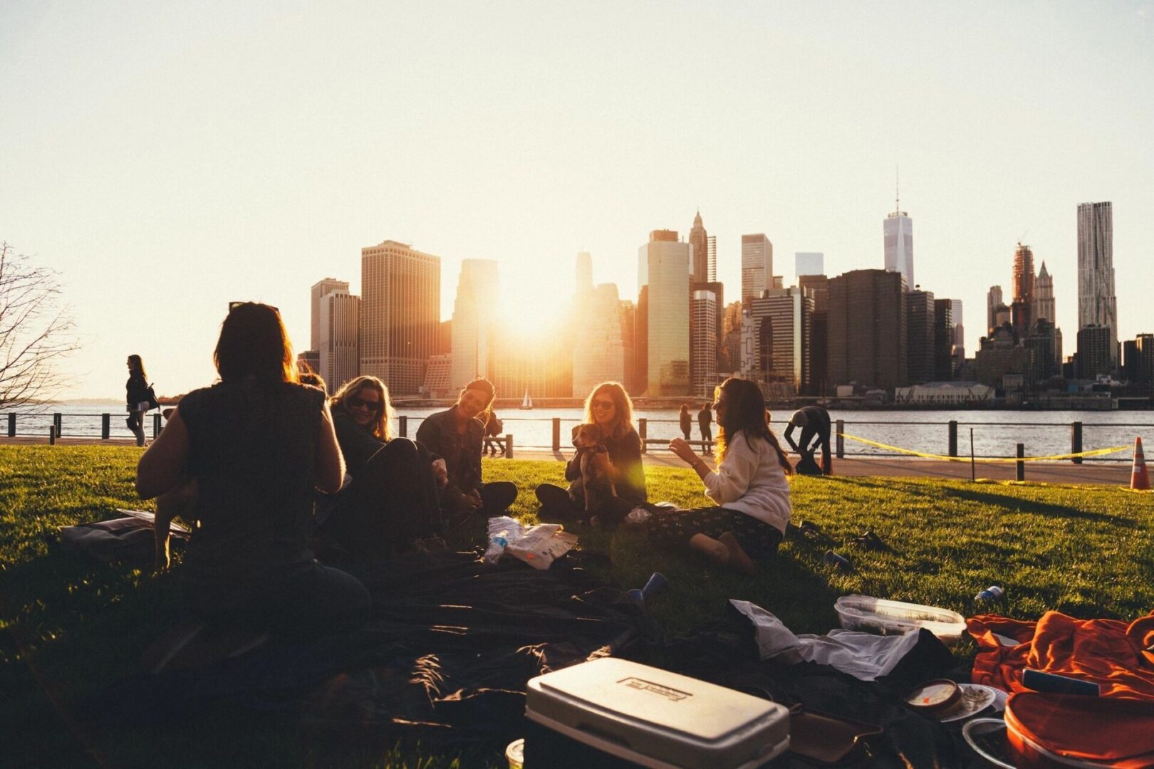 A group of people sitting on the grass near water.